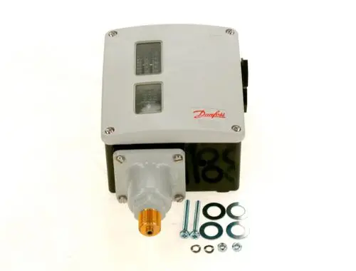 Danfoss Druckwächter in grauer Kunststoffgehäuse, mit zwei Anzeigefenstern, montiert an einem Anschluss mit Gewinde. Zubehörteile liegen daneben.